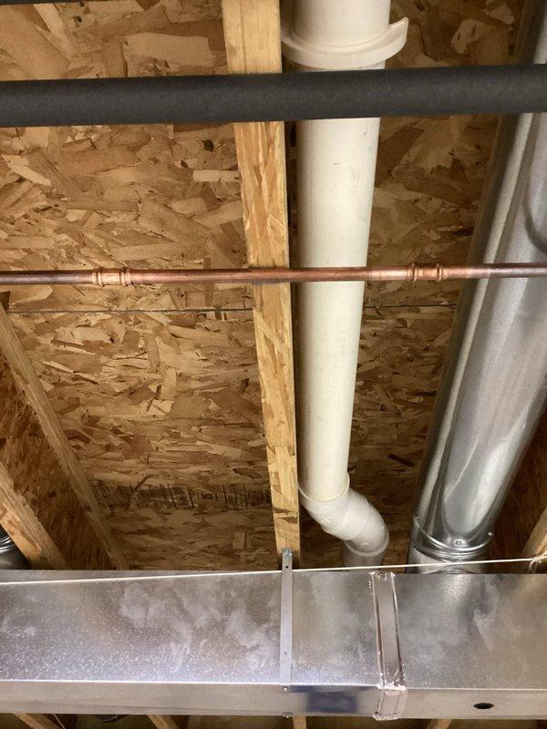 Responded to emergency call for leaky pipe in basement of 25-year-old residential property. Upon arrival, located active leak in copper water line running through unfinished basement ceiling area near HVAC ductwork and structural framing. Leak appeared recent, estimated to have been active for approximately 24 hours based on water accumulation and customer report. Shut off water supply to affected line, assessed damage to copper piping at failed joint connection, and repaired leak using appropriate coupling and soldering techniques. Verified repair integrity through pressure testing and restored water service. Inspected surrounding plumbing infrastructure, including adjacent PVC drain lines and insulated pipes, to ensure no additional leaks or compromised connections were present. Documented conditions with photographs showing exposed utilities, OSB sheathing, wooden framing members, and metallic ductwork in the work area for customer records.
