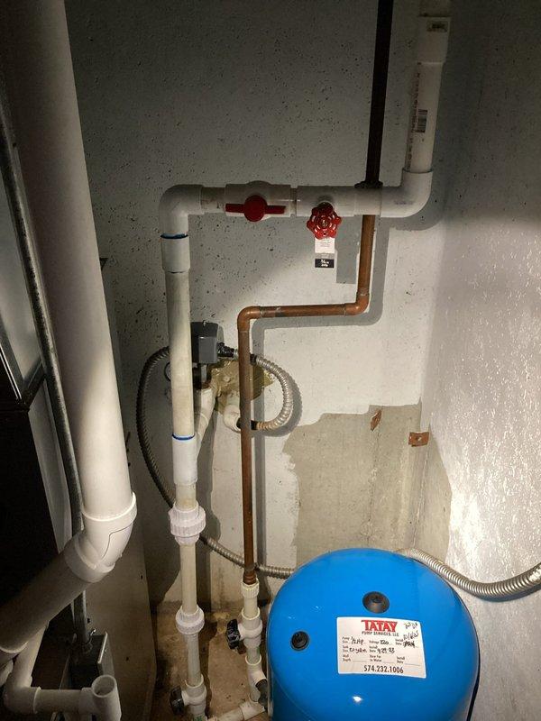 Responded to a follow-up water leak in the basement on the same pipe previously serviced. Upon inspection, identified a new leak located lower down on the copper piping assembly near the water heater system. Assessed the plumbing configuration, which included copper pipe connections, PVC components, gate valves, and an expansion tank. Documented the leak location with photographs showing the affected copper piping, valve assembly, and surrounding plumbing infrastructure for repair recommendations.