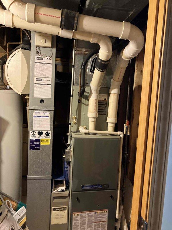 Conducted comprehensive HVAC replacement estimate for residential property with non-functional cooling system. Existing American Standard furnace and air conditioning unit assessed in utility closet installation, with system blowing air but failing to provide cooling. Evaluated current equipment configuration including furnace, water heater, and associated PVC condensate drainage piping. Documented significant wear, accumulated debris, corrosion, and mineral deposits on existing equipment base and components indicating age-related deterioration. Photographed equipment condition showing environmental exposure, dust accumulation, and maintenance history. Provided estimate options for complete HVAC system replacement including new air conditioning unit, furnace, and humidifier installation to restore proper heating and cooling functionality.