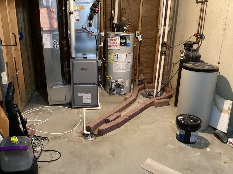 Responded to service call for reported water heater leak in basement with visible pudding around unit. Upon arrival, conducted thorough inspection of white cylindrical tanked water heater and surrounding plumbing connections. Examined all visible piping including copper supply lines, temperature and pressure relief valve, drain valve, and discharge tube for signs of active leakage or moisture accumulation. Inspected tank exterior for corrosion, rust staining, or structural compromise. Checked floor area beneath and around water heater to identify source and extent of water accumulation on concrete floor. Verified unit was currently operational and producing hot water as reported. Assessed age and condition of installation based on manufacturer labels and specifications visible on tank exterior. Evaluated all connection points, fittings, and valves for potential leak sources. Documented findings with photographic evidence showing mechanical room layout, water heater positioning relative