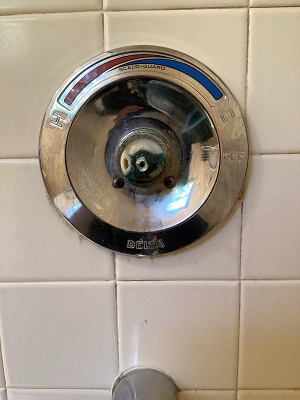 Responded to plumbing issues in a 33-year-old home including a toilet leak penetrating to the basement and a Delta Scald-Guard shower valve delivering only hot water regardless of temperature control adjustment. Inspected the shower valve assembly mounted on ceramic tile and accessed the crawl space/attic area to assess the toilet leak source, documenting the plumbing infrastructure including valve components and structural connections. Both issues had persisted for approximately two weeks prior to service call.