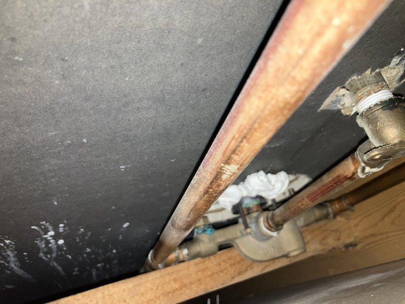 Responded to plumbing issues in a 33-year-old home including a toilet leak penetrating to the basement and a Delta Scald-Guard shower valve delivering only hot water regardless of temperature control adjustment. Inspected the shower valve assembly mounted on ceramic tile and accessed the crawl space/attic area to assess the toilet leak source, documenting the plumbing infrastructure including valve components and structural connections. Both issues had persisted for approximately two weeks prior to service call.