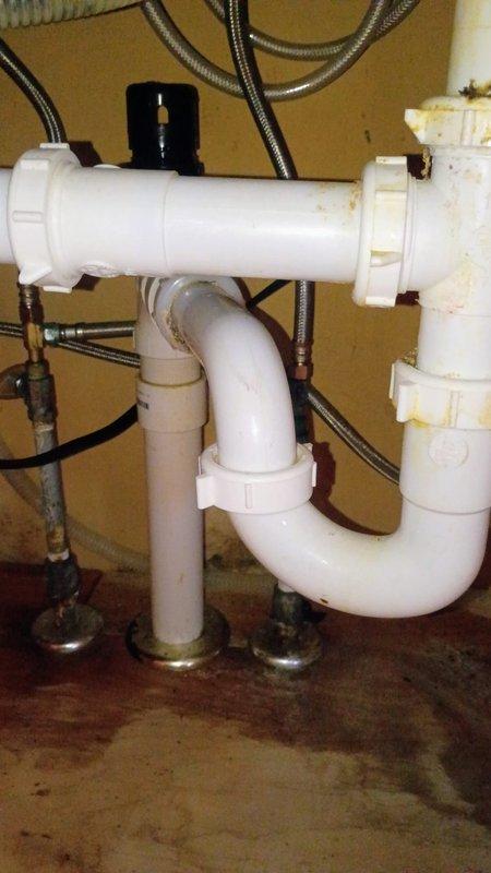 Provided comprehensive estimate for complete kitchen sink replacement in 1940s-era home. Assessed existing stainless steel double-basin sink with malfunctioning faucet, deteriorated basin condition showing significant mineral deposits and staining, and aging disposal unit on left compartment. Documented existing drain assembly including white PVC P-trap configuration, air admittance valve, and braided stainless steel supply lines showing wear and discoloration. Estimate includes removal and replacement of double-compartment sink, faucet assembly with handles and spray attachment, garbage disposal, complete drain piping system including new P-trap, and connection to main kitchen drain line beneath granite countertop.