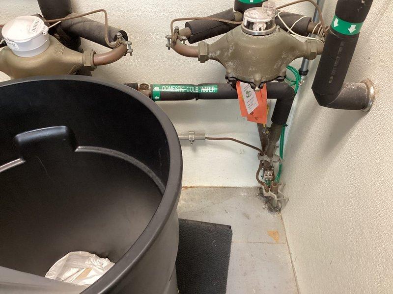 Responded to a water leak in the mechanical room originating from a failing ball valve at the water meter assembly. Upon arrival, found active leak being contained in a bucket with water supply still operational. Inspected the domestic cold water system including backflow preventer assembly and associated piping. Documented the defective ball valve with corrosion present on metal fittings and provided quote for repair work to be scheduled after hours per customer request.