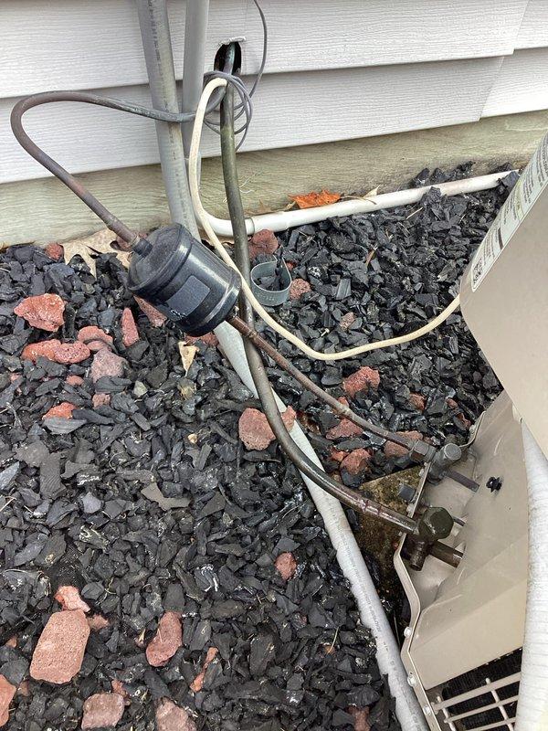 # HVAC Maintenance - Planned Single Maintenance

Completed comprehensive air conditioning maintenance inspection on residential outdoor condensing unit. Performed visual assessment of refrigerant line set, noting weathered gray foam insulation on suction line with signs of UV degradation and age-related deterioration. Inspected copper refrigerant lines for proper routing and support, observing surface oxidation consistent with normal outdoor exposure. 

Examined electrical conduit and wiring connections running to condensing unit, verifying secure mounting to exterior wall. Assessed white PVC condensate drain line for proper pitch and drainage functionality. Verified unit positioning on gravel pad with adequate clearance from building structure. Inspected manufacturer label and unit specifications for reference during maintenance procedures. All refrigerant lines properly insulated and secured with appropriate mounting brackets. System installation shows typical aging characteristics b