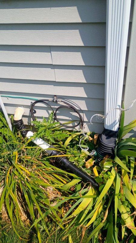 Responded to water leak call regarding exterior pipe with hole ejecting water when sump pump activates. Upon arrival, inspected exterior plumbing system partially obscured by dense vegetation near building foundation. Located damaged black flexible discharge line connected to sump pump system with visible hole causing water ejection during pump cycle. Assessed water heater and associated plumbing connections in mechanical room to verify no additional leaks in system. Documented condition of damaged sump pump discharge pipe and surrounding equipment. Water service remained on during inspection as no standing water was present and leak was isolated to exterior discharge line during pump operation only.