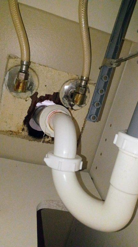 Provided plumbing components for under-sink installation including white PVC P-trap assembly with threaded fittings and braided stainless steel supply lines with shutoff valves. Customer purchased materials to replace heavily corroded metal drain pipes and deteriorated fixtures showing extensive rust and oxidation damage beneath existing sink.