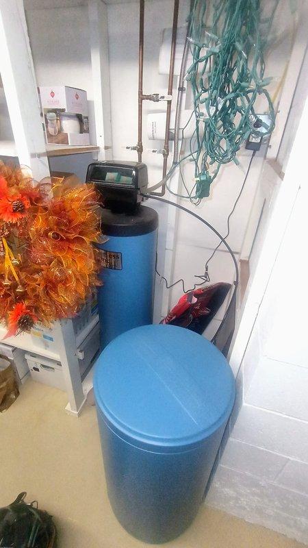 Responded to service call for water softener system reported as non-functional after 13+ years of operation. Upon arrival, performed diagnostic inspection of dual-tank water treatment system including visual assessment of control valve assembly, plumbing connections, and system components. Examined black control head with copper piping connections, verified pressure ratings on system components (150°F/194 PSI), and inspected braided stainless steel supply lines and brass fittings for proper installation and potential leaks. Assessed brine tank condition and salt levels, checked for proper water flow through resin tank, and evaluated electrical connections to control valve. Documented equipment configuration and current system status with photographic evidence showing installation setup beneath water heater area and main utility room location. Provided customer with findings regarding system operation and recommended next steps for restoring proper water softening functionality.