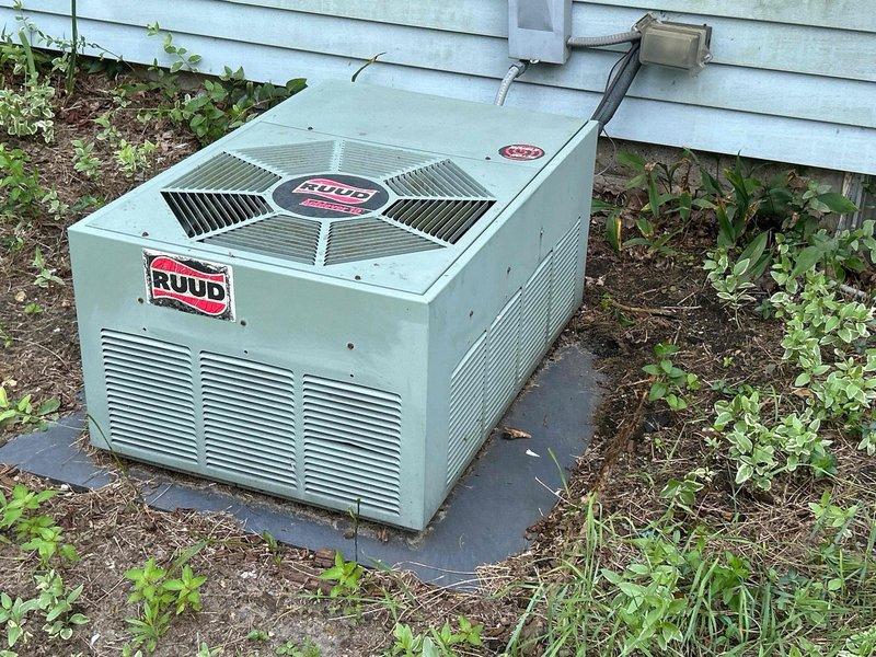 Conducted comprehensive site evaluation for complete HVAC system replacement at residential property. Assessed existing Ruud outdoor condensing unit positioned on concrete pad adjacent to exterior wall, noting standard refrigerant line routing and electrical disconnect configuration. Documented current equipment specifications, installation conditions, and electrical service panel capacity to determine compatibility requirements for new system installation. Evaluated electrical panel with dual-column breaker configuration and circuit distribution to ensure adequate amperage availability for replacement equipment. Photographed existing equipment placement, clearances, and surrounding landscape conditions to develop accurate replacement proposal and identify any site preparation needs prior to installation.