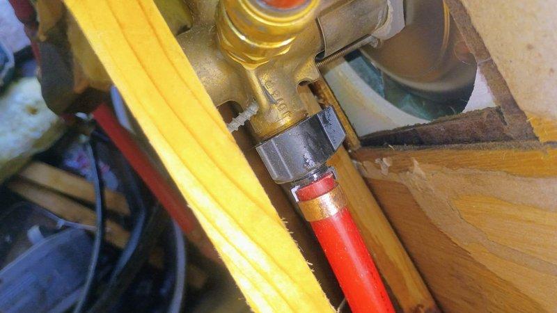 Responded to emergency plumbing call at mobile home where access door to water pipe compartment had failed and pipe was actively flowing water prior to arrival. Upon arrival, water supply had been shut off by customer to prevent further discharge. Performed diagnostic inspection of plumbing infrastructure in crawlspace access area, identifying compromised PVC piping connections and fittings. Examined brass valve assembly with connected flexible supply lines and assessed condition of threaded connections at P-trap and elbow joints. Inspected surrounding wooden framing and insulation for water damage or saturation. Documented all plumbing components including white PVC drainage pipes, brass shutoff valves, and flexible red supply hoses with securing clamps. Verified integrity of all visible pipe connections and fittings in confined utility space. Provided recommendations for necessary repairs to restore water service safely.