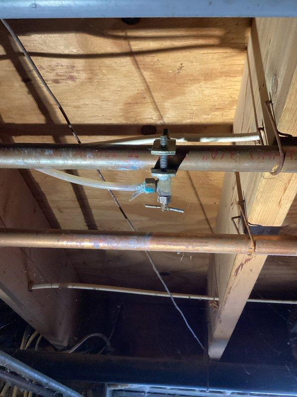 Responded to water leak in basement originating from copper piping above furnace humidifier. Inspected plumbing infrastructure in ceiling joists and identified leak at T-joint fitting in copper supply line. Assessed humidifier installation and associated water feed connections, including solenoid valve and brass fittings with integrated electrical controls. Advised customer of diagnostic findings and service fee for evaluation.