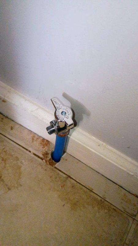 Installed new water supply line from basement to refrigerator location. Ran copper piping through ceiling joists and wall cavity, terminating with a blue-handled ball valve shutoff featuring 1/4" compression fitting at the point of connection. Applied thread sealant at all connection points to ensure leak-free operation and mounted shutoff valve securely to baseboard for easy access.