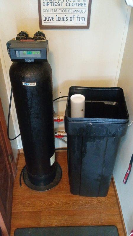 Responded to water backup issue at residential water softener system. Upon arrival, inspected 2-year-old water softening unit consisting of black resin tank with digital control head and blue-gray brine cabinet. Evaluated plumbing connections, bypass valves, and drain line for blockages or restrictions causing localized backup in softener area. Examined brine tank for proper salt levels and checked for potential drain line clogs or improper drainage that would prevent regeneration cycle completion. Verified system was isolated issue and not affecting whole-house plumbing. Documented existing installation with photos showing control head display, valve connections, and overall system condition for service records.