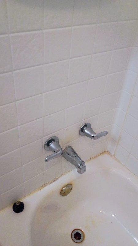 Responded to service call for non-functioning tub spout on wall-mounted chrome faucet assembly. Upon inspection, identified inoperative spout with visible signs of deterioration along tub-to-wall junction including rust staining, mineral deposits, and compromised caulking. Performed diagnostic assessment of three-piece tub faucet system including handles, spout, and overflow assembly. Addressed water flow issues and cleaned affected areas to restore proper functionality. Documented existing conditions including surface staining on tub, discolored grout lines, and aging caulk requiring future maintenance attention.