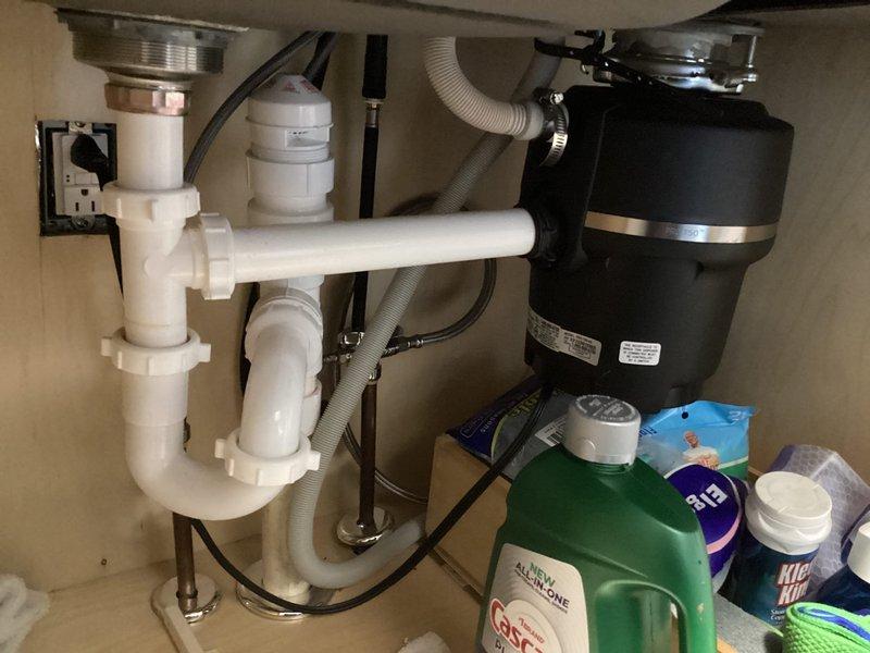 Responded to kitchen water leak caused by disconnected pipes beneath the sink. Upon arrival, inspected the under-sink plumbing configuration which included white PVC P-trap assembly, chrome tailpiece, garbage disposal unit with flexible gray corrugated drain hoses, and associated drain connections. Reconnected and secured the disconnected drain pipes, tightened all slip-joint connections on the P-trap assembly, and verified proper alignment of the garbage disposal discharge line. Tested all connections for leaks by running water through the system and confirmed proper drainage with no active leaks present upon completion.