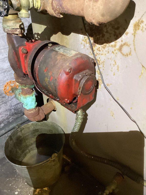 Responded to service call for boiler system discharging water from pressure relief valve during operation. Upon arrival, inspected boiler system and associated components including circulator pump, pressure gauge, and relief valve assembly. Found circulator pump showing significant wear and age-related deterioration with paint loss exposing bare metal. Verified system pressure readings on wall-mounted gauge indicating potential overpressure condition. Documented existing conditions with photographs showing worn red circulator pump with copper piping connections displaying corrosion and oxidation, collection bucket positioned beneath unit to catch discharge. Assessed that pressure relief valve activation likely caused by circulation failure or expansion tank malfunction leading to excessive system pressure. Provided diagnostic findings to customer and discussed options for repair versus replacement. Customer requested quote for new boiler system installation as alternative to repairing 