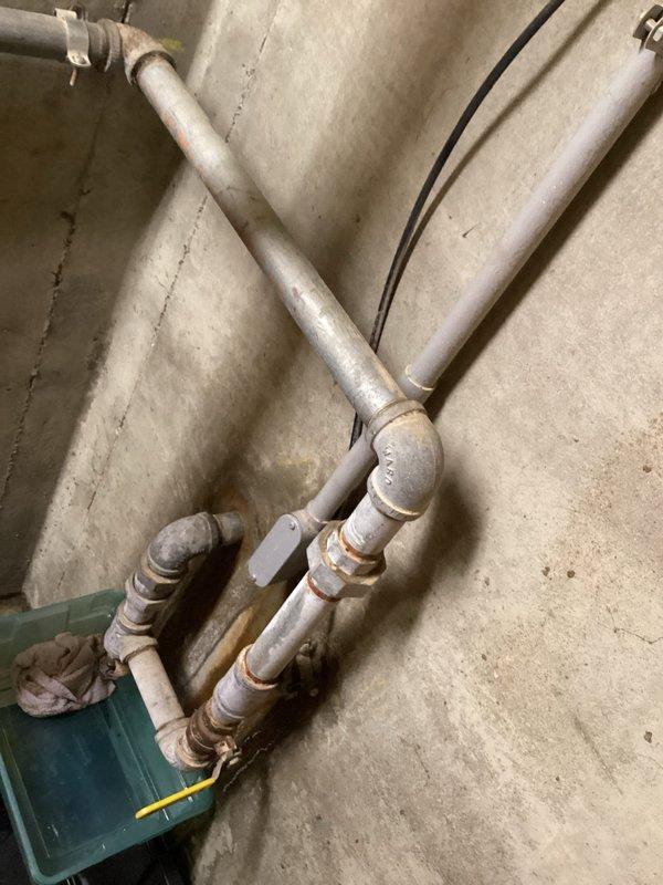 Responded to basement water leak complaint with 10-20 gallons daily accumulation against cement wall. Upon inspection, identified aged galvanized piping system mounted on basement wall displaying significant oxidation, rust staining at joints and fittings, and visible corrosion throughout. Documented deteriorated plumbing configuration and examined exterior property for potential water intrusion sources, noting cracked concrete patio sections and exterior drainage conditions that may contribute to moisture infiltration.