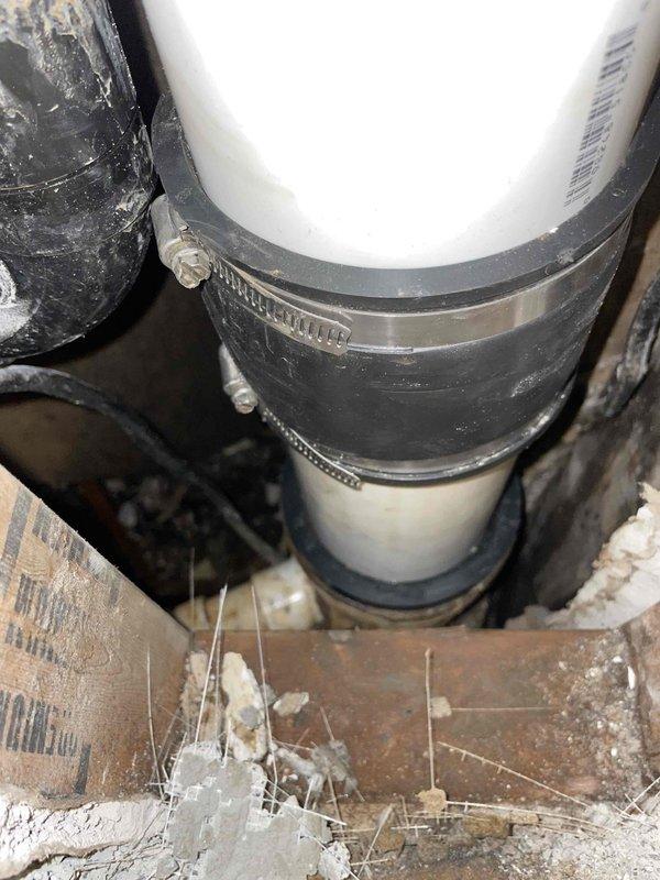Replaced deteriorated drain lines beneath flooring structure utilizing white PVC pipe with black rubber couplings and stainless steel hose clamps to ensure secure, leak-free connections. Addressed severe water damage discovered behind shower enclosure tile work, where prolonged moisture intrusion had compromised wooden framing and structural materials, evidenced by black discoloration and mold growth on exposed studs. Removed damaged tile section to access and remediate underlying deterioration, ensuring proper drainage system functionality and preventing further water infiltration into wall cavity.