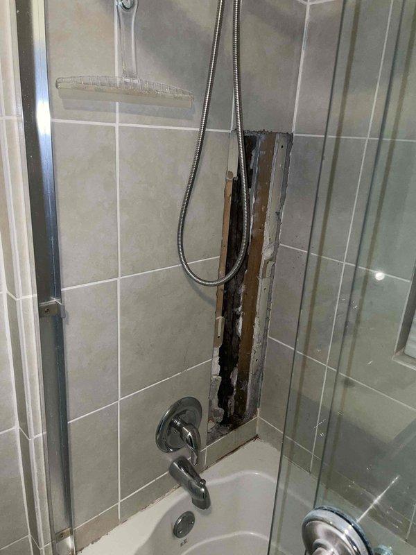 Replaced deteriorated drain lines beneath flooring structure utilizing white PVC pipe with black rubber couplings and stainless steel hose clamps to ensure secure, leak-free connections. Addressed severe water damage discovered behind shower enclosure tile work, where prolonged moisture intrusion had compromised wooden framing and structural materials, evidenced by black discoloration and mold growth on exposed studs. Removed damaged tile section to access and remediate underlying deterioration, ensuring proper drainage system functionality and preventing further water infiltration into wall cavity.