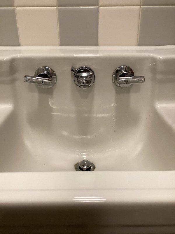 Responded to service call for bathroom sink faucet with reported leak and overly tight handle operation. Upon arrival, performed diagnostic inspection of wall-mounted three-piece chrome faucet assembly with dual lever handles and center pop-up drain control. Identified leak source and assessed handle mechanism requiring adjustment. Completed necessary repairs to resolve leak issue and adjusted tight handle to restore proper operation and ease of use. Verified all fixtures functioning correctly with no active leaks present upon completion.