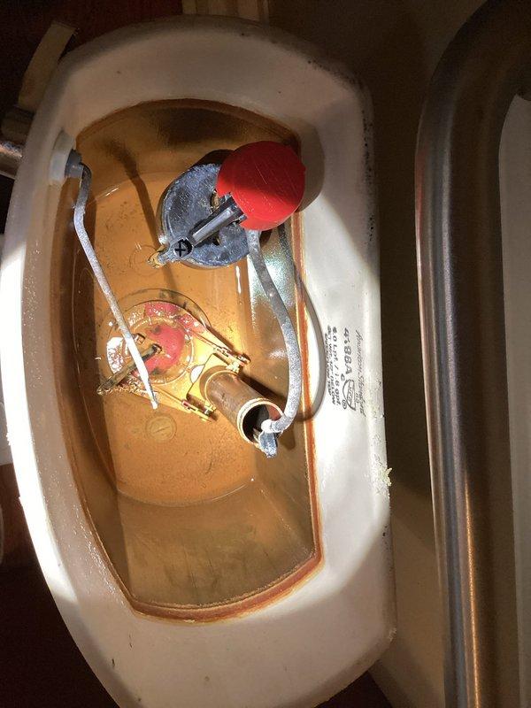 Responded to a toilet leak in a century-old home affecting one bathroom fixture. Upon inspection, removed tank lid and identified deteriorated flush valve components and discolored water indicating internal corrosion and mineral buildup. Documented existing flush mechanism with red float assembly, fill valve system, and brass flush valve showing signs of age-related wear, which was determined to be the source of the leak.
