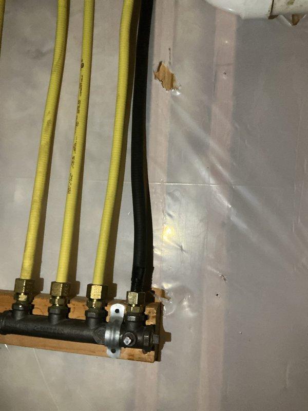 Replaced existing gas line with compliant installation featuring counterstrike protection to meet inspector requirements. Materials were procured and new gas piping was installed with proper manifold connections and securing methods, documented with photos showing the completed installation with yellow gas lines, black manifold assembly with brass fittings, and proper wall mounting.
