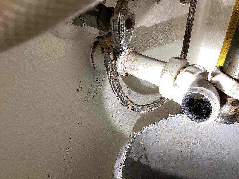 Responded to urgent call for slow-draining bathroom sink on shop floor. Initial attempt to clear blockage by removing and cleaning P-trap was unsuccessful in resolving drainage issue. Conducted thorough inspection of drain assembly and accessible plumbing components beneath sink, including PVC drain piping, trap configuration, and supply line connections. Documented existing conditions of drainage system showing age-related discoloration and mineral deposits on fixtures. Inspected associated plumbing infrastructure including corroded metal pipes, valves, and water heater connections displaying significant rust and oxidation. Photographed all plumbing components for service records. Blockage determined to be located beyond P-trap in main drain line, requiring additional drain cleaning equipment or methods to fully resolve slow drainage condition.