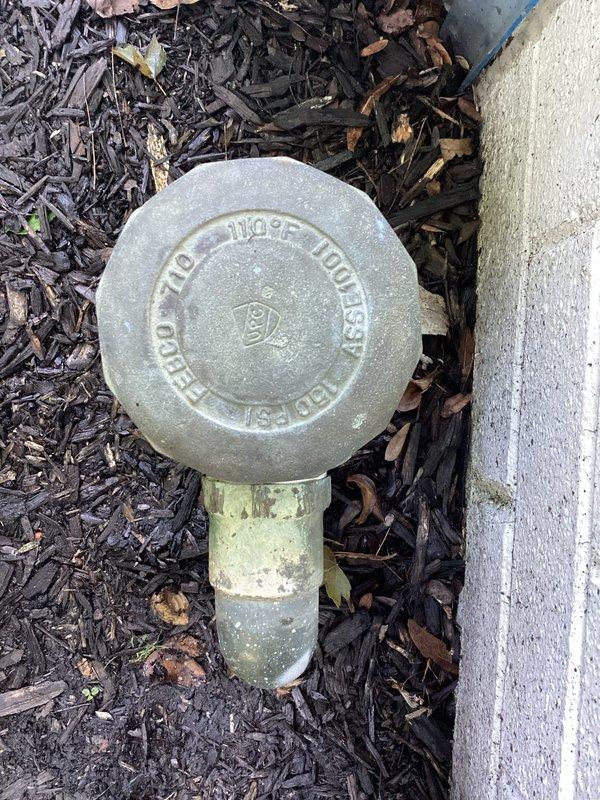 Responded to service call for leaking outdoor water spigot located near building foundation. Upon arrival, inspected exterior hose bib assembly and main water shutoff valve positioned at ground level against exterior wall. Valve assembly showed significant weathering, corrosion, and patina consistent with age and prolonged outdoor exposure. Identified leak source at spigot connection point. Replaced defective outdoor spigot with new frost-free hose bib assembly. Tested system for proper operation and verified no additional leaks present at valve stem or shutoff assembly. System restored to full functionality.