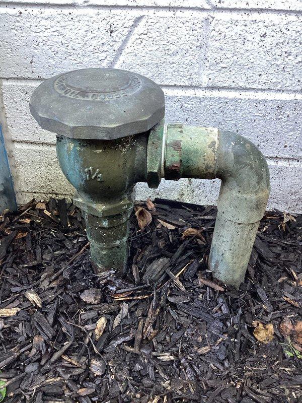 Responded to service call for leaking outdoor water spigot located near building foundation. Upon arrival, inspected exterior hose bib assembly and main water shutoff valve positioned at ground level against exterior wall. Valve assembly showed significant weathering, corrosion, and patina consistent with age and prolonged outdoor exposure. Identified leak source at spigot connection point. Replaced defective outdoor spigot with new frost-free hose bib assembly. Tested system for proper operation and verified no additional leaks present at valve stem or shutoff assembly. System restored to full functionality.