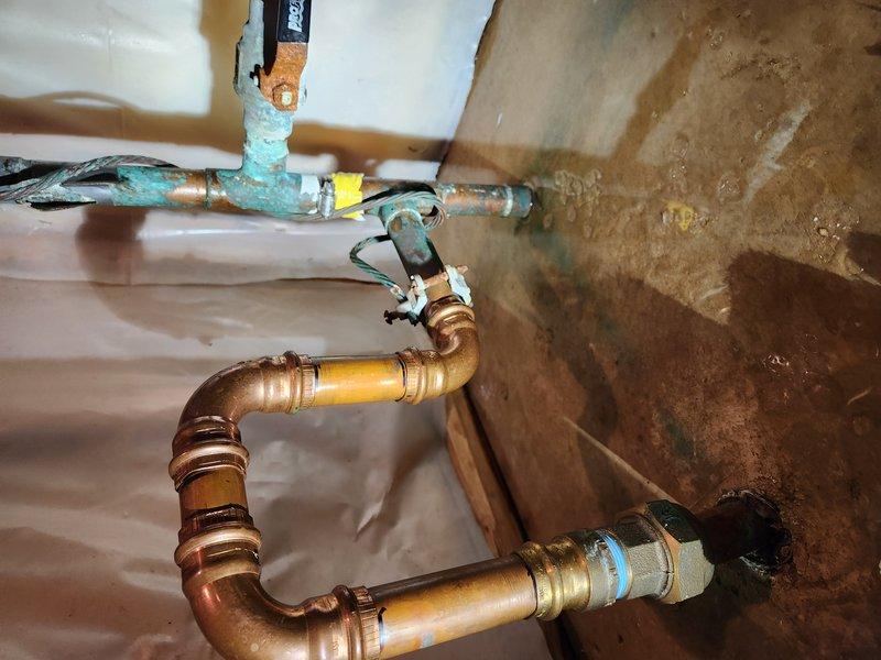Responded to emergency water leak in basement where copper piping was actively dripping and spraying water. Upon arrival, found standing water present and main water supply still active. Located leak source at copper pipe assembly near shutoff valves. Shut off water supply to stop active leak and prevent further water damage. Assessed plumbing configuration including U-trap copper assembly and associated shutoff mechanisms. Documented existing conditions showing water staining on surfaces and moisture barrier, indicating ongoing leak had compromised the area. Evaluated copper piping connections, joints, and fittings for integrity and identified failed connection point requiring repair.