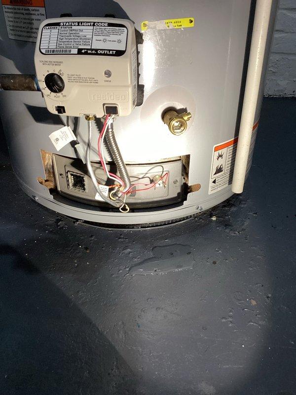 Responded to service call for 7-year-old tanked water heater with reported water leakage from bottom of unit and inoperative pilot light with no status light indication. Upon arrival, performed comprehensive diagnostic inspection of gas control valve, burner assembly, and tank integrity. Removed access panel to examine internal components including gas control valve with status light indicator, flexible gas line connector, and burner assembly with brass fittings and copper connections. Inspected expansion tank mounted on top of unit with flexible braided hoses and brass fittings, along with associated copper piping and PVC connections running to ceiling joists. Identified active leak originating from lower tank section and confirmed pilot light failure with non-functional status indicator on gas control valve. Assessed overall system configuration including plumbing connections, gas supply line, and venting arrangement. Documented conditions through photographic evidence showing compro