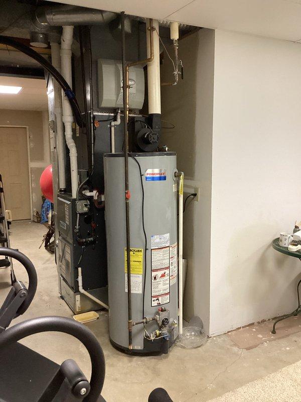 Responded to water leak in lower level basement utility area. Upon arrival, identified active leak from damaged pipe connected to water heater with customer-placed bucket collecting water. Inspected water heater plumbing assembly including copper supply lines, PEX distribution lines, and associated fittings. Documented compromised pipe section with hole causing water discharge. Assessed surrounding plumbing infrastructure including PVC drainage system, gas connections, and mounting hardware for additional concerns. Photographed affected area showing water heater, furnace, and complete piping configuration for repair documentation and customer records.