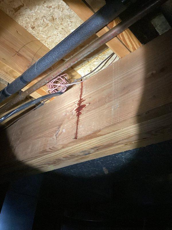 Responded to emergency water leak in basement following recent icemaker line rerouting to sink. Upon arrival, found active water flow with standing water present on basement floor and water damage visible on structural wooden beams above, indicated by reddish-brown staining. Shut off water supply to stop flooding. Inspected previously rerouted icemaker water line connection at sink and traced leak source through basement ceiling. Identified failed connection point causing water to discharge into basement cavity and onto concrete floor. Repaired compromised water line connection, pressure tested system to verify integrity of repair, and confirmed no additional leaks present. Advised on water damage assessment and recommended monitoring affected structural areas for further evaluation.
