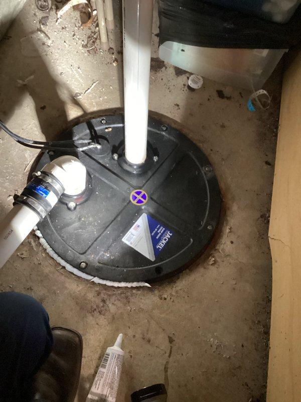 Responded to complaint of intermittent sewage odor in upstairs bathroom occurring when basement shower was in use. Inspected sump pump system and drainage connections in basement utility area. Found sump pump installation with PVC discharge piping and check valve assembly. Examined pump housing, discharge connections, and verified proper sealing of sump pit lid to prevent sewer gas escape. Documented existing equipment condition including pump assembly, electrical connections, and plumbing tie-ins. Advised on potential drain trap issues and venting concerns that could allow sewer gases to migrate between floors during water usage events.