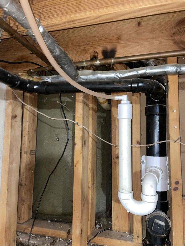 Conducted on-site assessment for shower installation project in downstairs bathroom. Evaluated existing bathroom layout featuring basket-weave tile flooring, mint green walls, and standard toilet fixture to determine optimal placement for new shower unit with surround. Documented current bathroom dimensions and configuration in narrow residential layout. Inspected basement ceiling area below bathroom to assess existing plumbing infrastructure, including white PVC drain lines, black waste pipes, and P-trap assembly. Identified accessible joists and framing for potential shower drain connection and water supply routing. Photographed exposed plumbing system and structural framing to develop accurate material list and labor estimate for complete shower installation with surround panels.