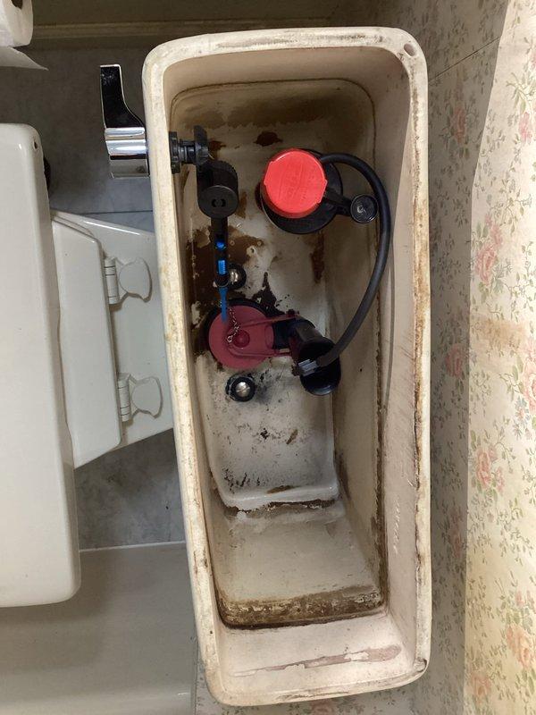 Completed toilet rebuild in commercial restroom facility. Removed existing tank components and installed new fill valve, flush valve assembly with red float mechanism, and flapper. Replaced corroded water supply shut-off valve with new fixture. Reset toilet with new wax ring seal to ensure proper connection to waste line. Tank interior showed significant age-related deterioration including rust staining and mineral deposits, which were addressed during component replacement. All internal mechanisms tested and verified operational upon completion.