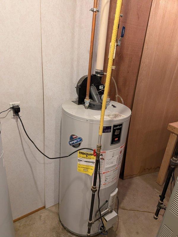 Responded to water leak emergency in basement area near water heater with standing water present on concrete floor. Upon arrival, water supply was already shut off by customer. Conducted thorough inspection of water heater installation, associated copper supply lines, PVC drainage system, and all visible plumbing connections including shutoff valves and brass fittings. Examined mounting brackets, rubber couplings, and mechanical systems in utility area to identify source of leak causing dark discoloration on cement floor. Documented existing conditions of water heater unit, flexible gas connector line, drainage pipes, and surrounding plumbing infrastructure through photographic evidence for diagnostic purposes.