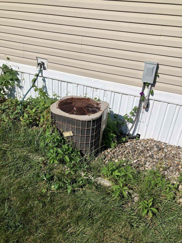 Conducted on-site evaluation of existing HVAC system in manufactured home for complete furnace and air conditioner replacement estimate. Inspected 25-year-old original equipment including outdoor condenser unit and indoor furnace components. Documented current system conditions through photographs showing exterior cylindrical condenser with weathered top grille, wire mesh protection, and adjacent electrical disconnect box, as well as interior access panel for furnace evaluation. Assessed equipment age, system compatibility requirements, and installation considerations specific to manufactured home construction. No active system failures reported at time of visit. Provided comprehensive replacement options and equipment recommendations based on home specifications and current system configuration.