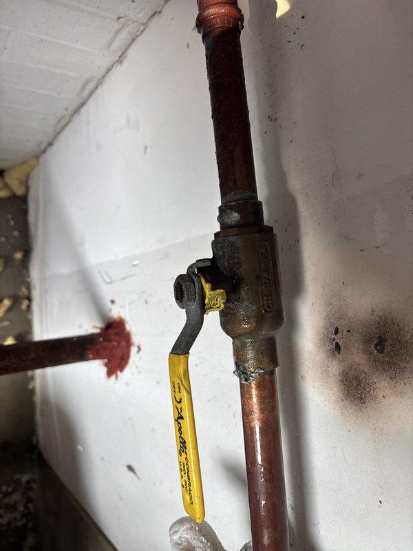 # Boiler System Pipe Repair

Responded to emergency call for actively leaking 1-inch pipe on boiler system causing property damage. Upon arrival, confirmed water supply had been shut off by occupant. Conducted thorough inspection of boiler system components, including copper piping, gas valve assembly, and potable water expansion tank installation.

Assessed condition of aged copper piping showing significant oxidation and patina buildup throughout the system. Examined brass gas valve with yellow handle and associated connections for integrity and proper function. Inspected potable water expansion tank mounted in utility area, verifying all electrical connections, wiring, and associated plumbing fittings. 

Documented existing system conditions including corrosion on pipe surfaces, valve body oxidation, and overall age of installation. Photographed all relevant components including vertical and horizontal copper pipe runs, valve assembly, expansion tank, and surrounding utility space c