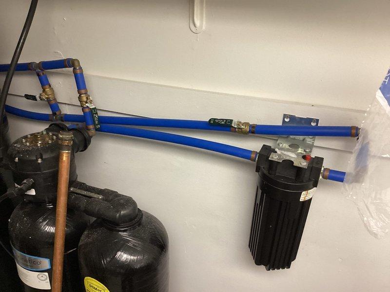 Responded to service call for 5-year-old tanked water heater reported as non-operational with strange odor and no visible leaks. Upon arrival, performed diagnostic inspection of water heater system and associated plumbing infrastructure. Evaluated copper supply lines with insulation, brass compression fittings, and connections. Inspected water treatment system including expansion tanks, PEX distribution lines, and whole-house filtration assembly mounted on wall. Examined control device and monitoring equipment connected to the system. Assessed all visible components including pressure vessels, brass fittings, and blue PEX tubing connections. Documented existing conditions with photographic evidence showing plumbing configuration, filtration hardware, and mechanical room setup for diagnostic purposes and future reference.