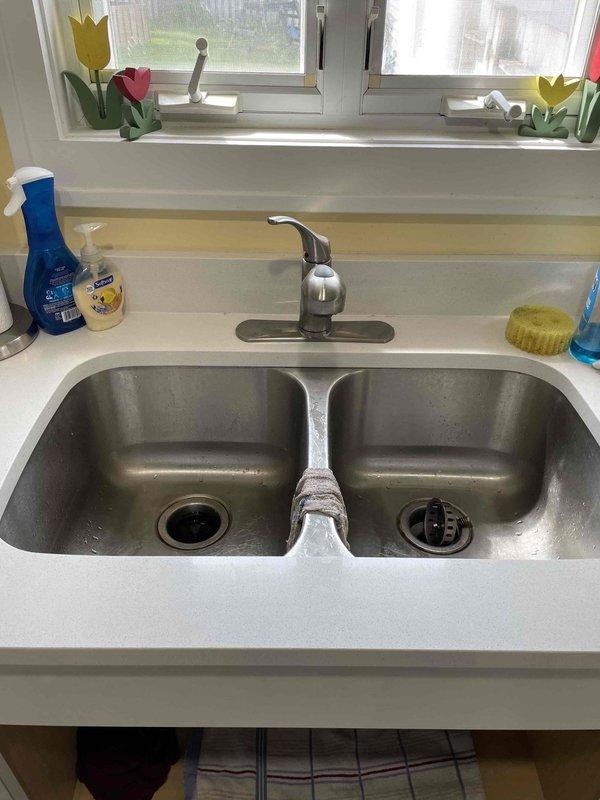 Responded to callback for persistent kitchen sink leak with water now appearing on countertop. Upon inspection, identified leak originating from under-sink plumbing assembly. Examined double-basin stainless steel sink configuration with garbage disposal unit connected to white PVC P-trap drainage system. Tightened slip-joint connections on drain pipes and verified proper sealing at all connection points. Inspected garbage disposal mounting and discharge connections for potential leak sources. Tested water supply lines and checked flexible hose connections for integrity. Ran water through both basins and disposal unit to verify leak repair and confirm no further water intrusion at countertop level or cabinet base. System operating properly upon completion.