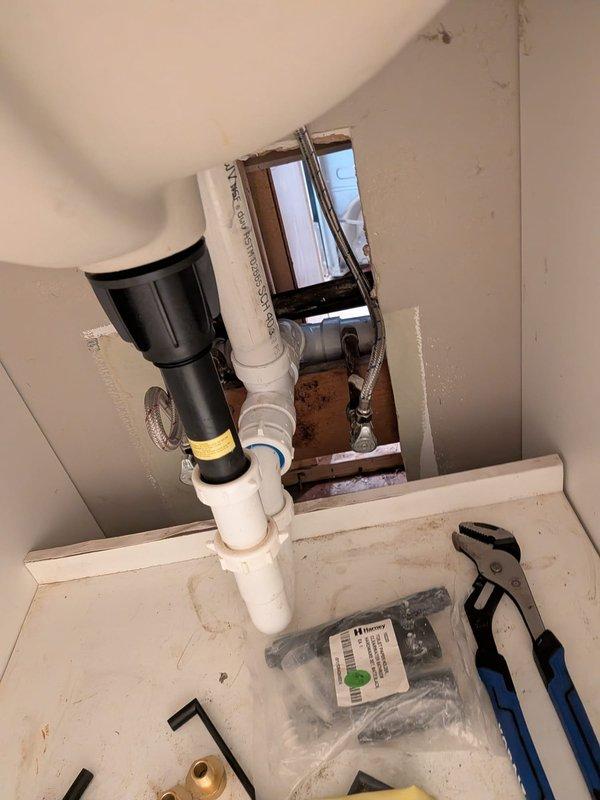 Responded to water leak located inside wall between bathroom and kitchen. Upon arrival, water supply was still active with minor standing water present. Accessed plumbing system through bathroom vanity cabinet and inspected P-trap assembly and drain connections. Investigated wall cavity and attic space to trace source of leak along copper supply lines. Located compromised pipe section within insulated copper water lines running through ceiling joists. Shut off main water supply to prevent further damage. Prepared replacement plumbing components and tools for repair work. Documented existing conditions of under-sink plumbing configuration, P-trap installation, and overhead copper piping with foam insulation in attic cavity for repair assessment and customer approval.