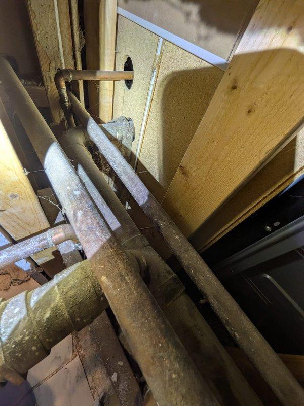 Responded to water leak located inside wall between bathroom and kitchen. Upon arrival, water supply was still active with minor standing water present. Accessed plumbing system through bathroom vanity cabinet and inspected P-trap assembly and drain connections. Investigated wall cavity and attic space to trace source of leak along copper supply lines. Located compromised pipe section within insulated copper water lines running through ceiling joists. Shut off main water supply to prevent further damage. Prepared replacement plumbing components and tools for repair work. Documented existing conditions of under-sink plumbing configuration, P-trap installation, and overhead copper piping with foam insulation in attic cavity for repair assessment and customer approval.