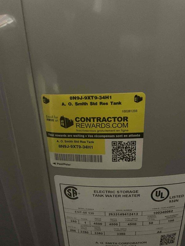 Installed A.O. Smith ENT 60 130 electric storage tank water heater in basement utility room per approved quote. Unit features 4500-watt heating element with 3380-volt capacity, copper piping connections at top, and white plastic tubing for proper drainage. Water heater was positioned adjacent to existing water softener system in narrow utility space with concrete block walls, ensuring adequate clearance for service access and code compliance.