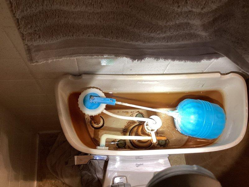 Responded to second level bathroom for reported toilet leak at base. Upon inspection, identified water seepage from bottom of toilet fixture. Removed tank lid and assessed internal components, noting significant rust discoloration in water supply, mineral deposits throughout tank interior, and deteriorated hardware consistent with hard water conditions. Diagnosed leak originating from compromised wax ring seal at toilet base due to age and mineral buildup affecting proper seating.