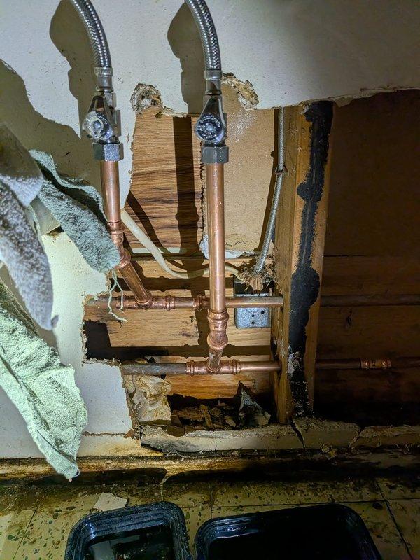 Responded to water leak emergency under bathroom sink. Upon arrival, found extensive water damage to wall cavity and surrounding structure, with significant deterioration of drywall and evidence of prolonged moisture intrusion. Existing shut-off valve had failed, causing active leak condition.

Removed damaged drywall sections to access plumbing infrastructure and assess full extent of damage. Shut down water supply to affected area. Removed old corroded shut-off valve showing green patina oxidation and signs of failure at compression fittings. Installed new chrome shut-off valve with proper compression fittings on vertical copper supply lines. Connected braided stainless steel flexible supply lines to new valve assembly, ensuring secure connections at all junction points. Tested system for leaks under full pressure and verified proper operation of new shut-off valve. Left exposed plumbing accessible for customer inspection and future drywall repair work.