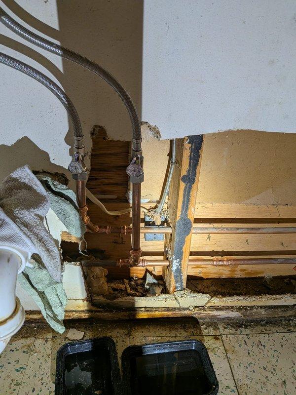 Responded to water leak emergency under bathroom sink. Upon arrival, found extensive water damage to wall cavity and surrounding structure, with significant deterioration of drywall and evidence of prolonged moisture intrusion. Existing shut-off valve had failed, causing active leak condition.

Removed damaged drywall sections to access plumbing infrastructure and assess full extent of damage. Shut down water supply to affected area. Removed old corroded shut-off valve showing green patina oxidation and signs of failure at compression fittings. Installed new chrome shut-off valve with proper compression fittings on vertical copper supply lines. Connected braided stainless steel flexible supply lines to new valve assembly, ensuring secure connections at all junction points. Tested system for leaks under full pressure and verified proper operation of new shut-off valve. Left exposed plumbing accessible for customer inspection and future drywall repair work.