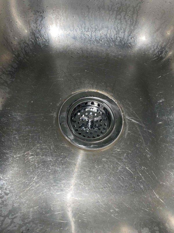 Completed quoted plumbing work involving removal of existing garbage disposal unit from kitchen sink drain assembly and replacement of deteriorated toilet shut-off valve. The existing shut-off valve exhibited significant age-related corrosion with visible patina on copper supply pipe and compromised functionality. Installed new chrome shut-off valve with braided stainless steel supply line connection to ensure proper water flow control and prevent potential leak issues. Kitchen sink drain opening restored to standard configuration following disposal removal, with drain assembly left clean and operational.