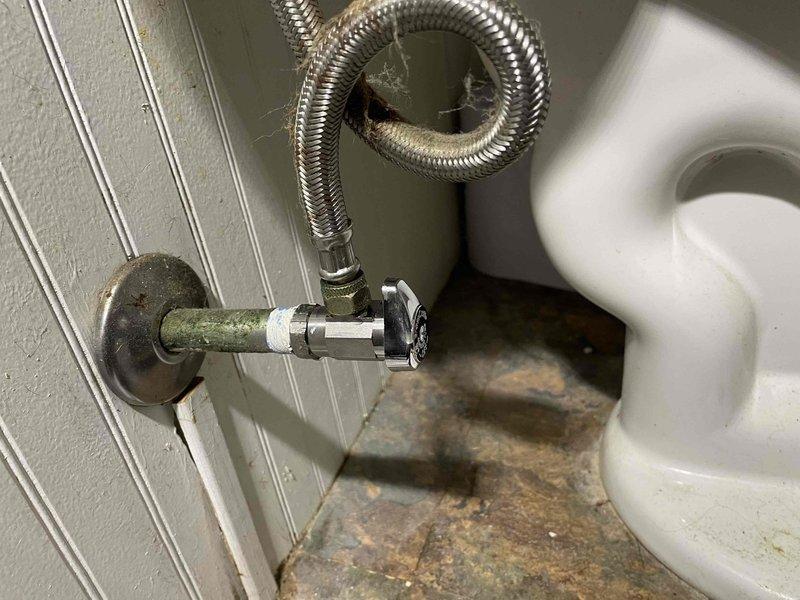 Completed quoted plumbing work involving removal of existing garbage disposal unit from kitchen sink drain assembly and replacement of deteriorated toilet shut-off valve. The existing shut-off valve exhibited significant age-related corrosion with visible patina on copper supply pipe and compromised functionality. Installed new chrome shut-off valve with braided stainless steel supply line connection to ensure proper water flow control and prevent potential leak issues. Kitchen sink drain opening restored to standard configuration following disposal removal, with drain assembly left clean and operational.