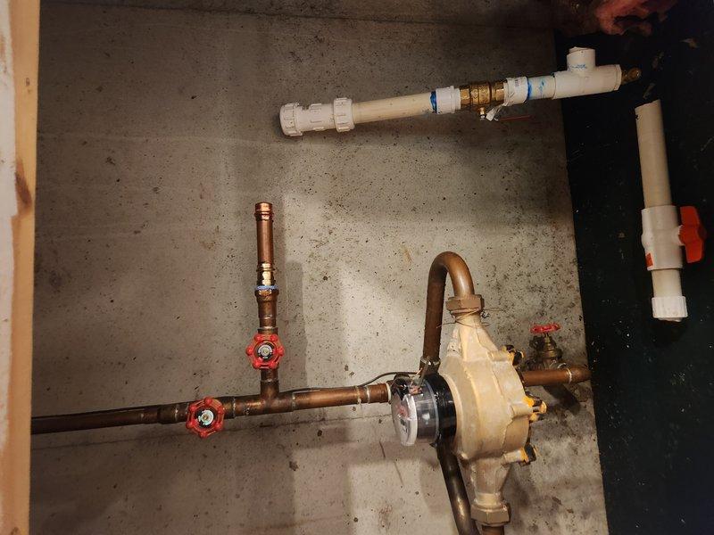 Responded to active water leak in basement with standing water present. Upon arrival, water supply was already shut off by customer. Inspected plumbing system and identified leak source in copper piping connected to sump pump assembly. System includes pump with clear housing, multiple copper lines with red-handled shut-off valves, and white PVC discharge piping with brass fittings and check valve. Documented existing installation showing proper configuration of shut-off valves and pump connections. Assessed standing water conditions and verified water supply remained isolated to prevent further flooding while awaiting repair authorization.